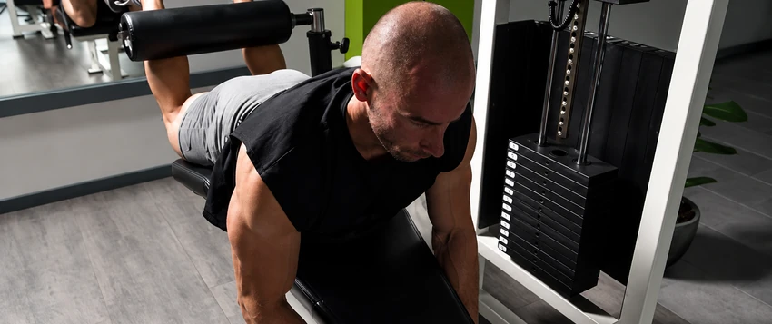 Man performing a controlled leg curl exercise in a gym while using progressive overload training principles