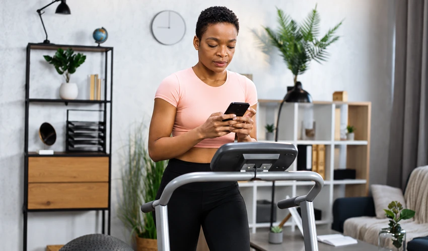 Woman tracking her workout progress on a smartphone during a home treadmill session