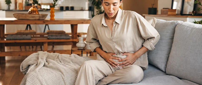 Woman sitting on a sofa holding her abdomen while experiencing bloating and stomach discomfort