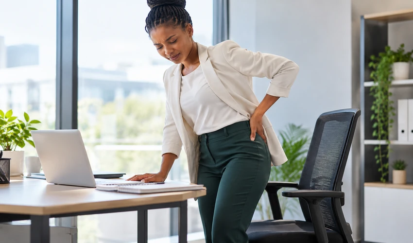 Office worker holding her hip while standing beside her desk, illustrating hip stiffness after prolonged sitting